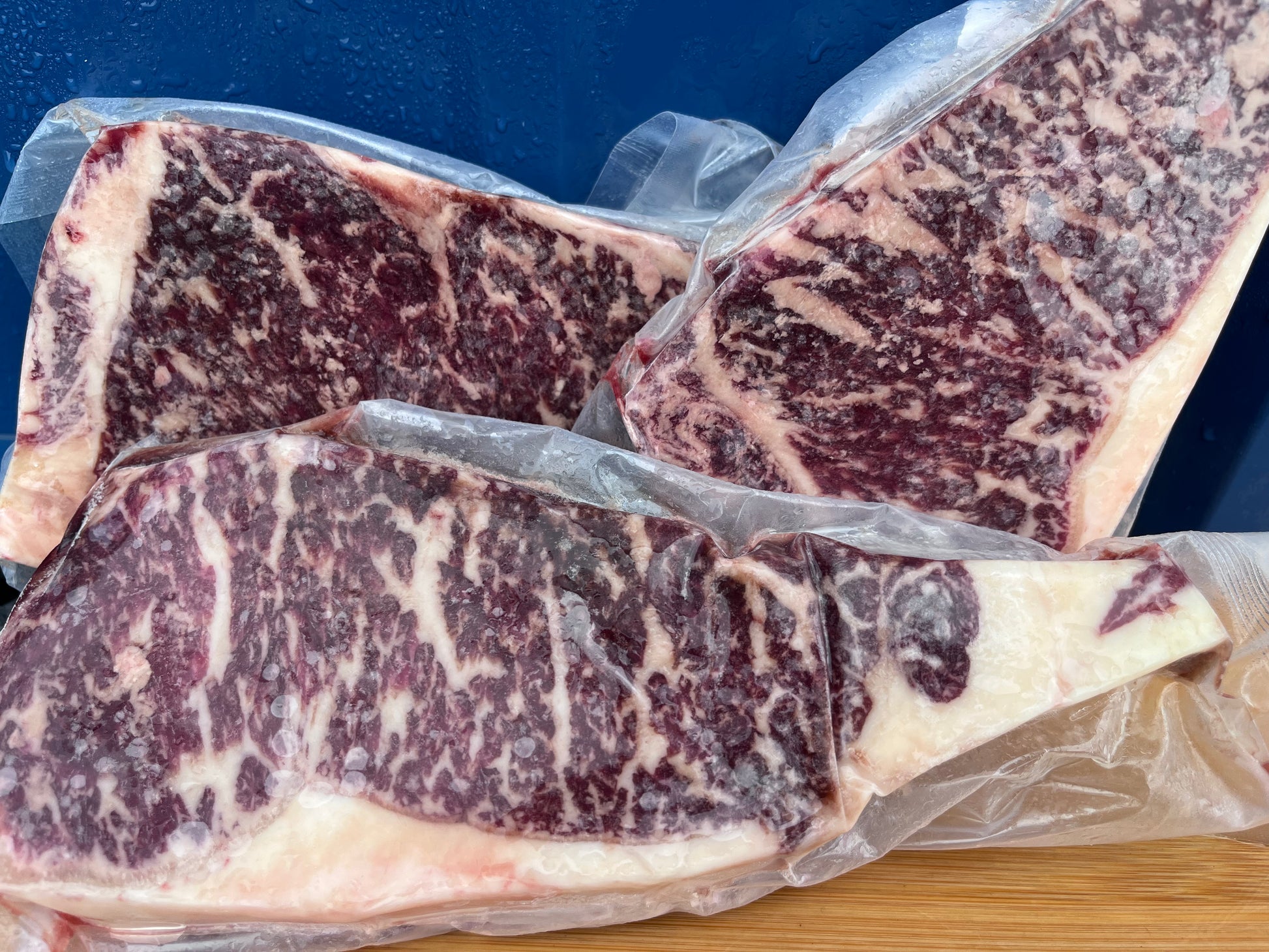 Three pieces of marbled raw beef on a blue background